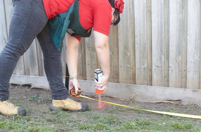 A person marking the ground with spray paint underneath a string line