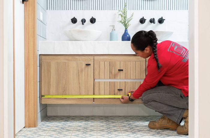 A Bunnings Team Member is measuring a bathroom vanity to plan LED strip light placement