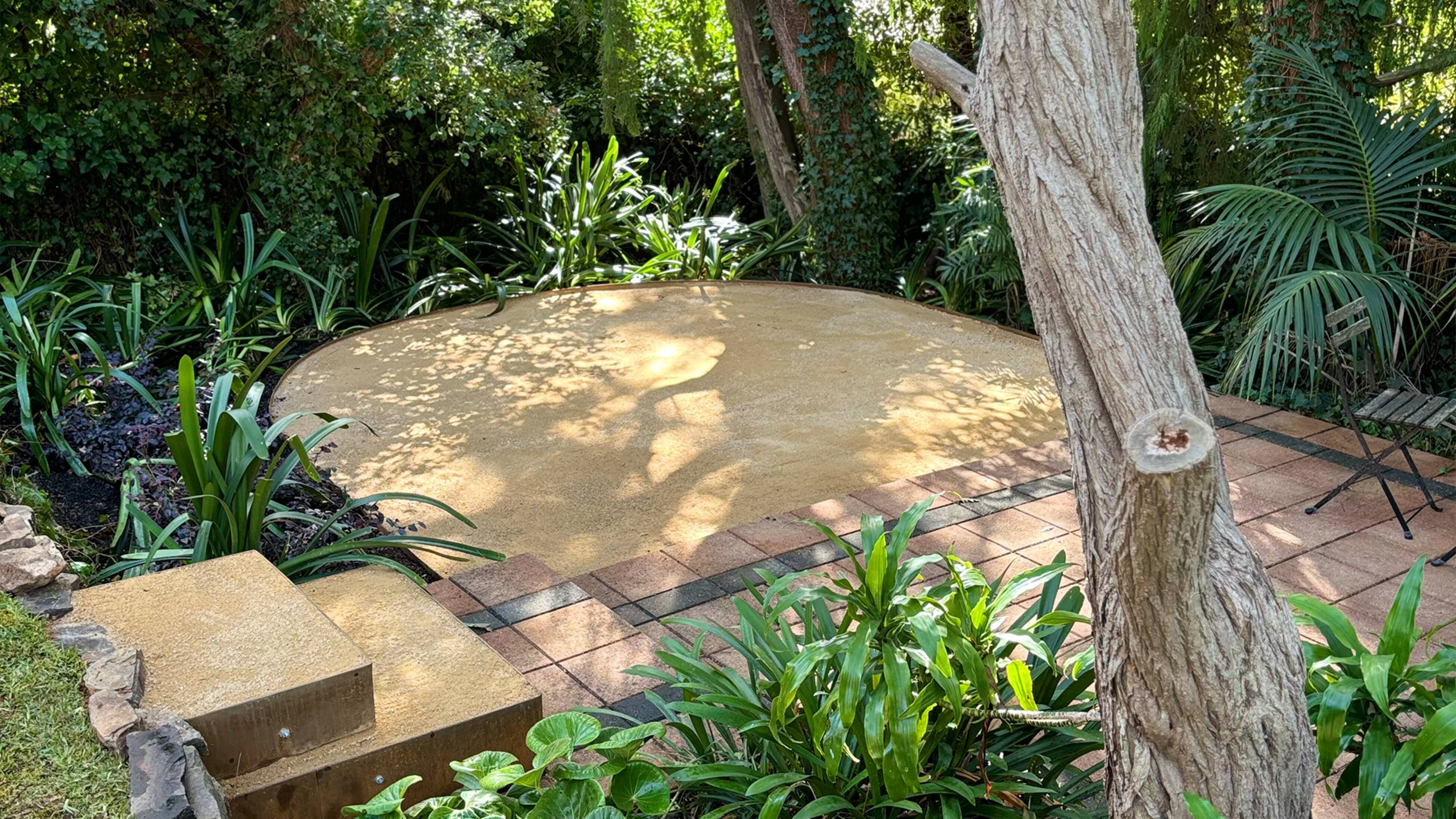 A lush green garden setting with pavers and raised steps showing a layered backyard design trend