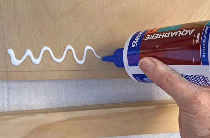 A hand applying a bead of adhesive to a piece of plywood.