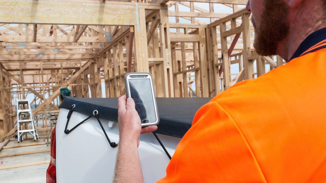 A tradesperson uses their smartphone at a timber-framed build.