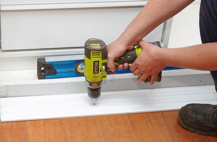 A person fixing a bottom track to the floor using a cordless driver