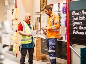 A tradie and a Bunnings Team Member in high-visibility clothing have a conversation in the plumbing section instore.
