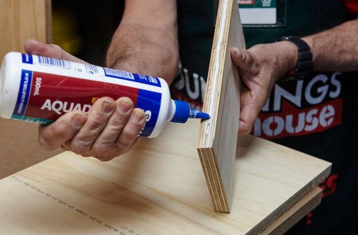 A person applying glue to the edge of a piece of plywood