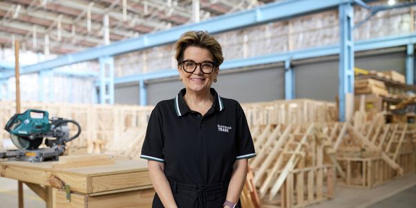 Bunnings Trade team member standing in a timber construction training workshop with woodworking equipment and timber framing in the background.