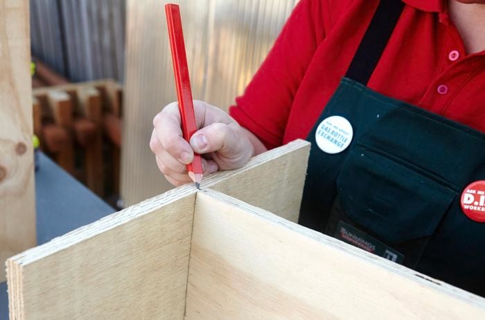 A person marking where two sheets of plywood make a T joint