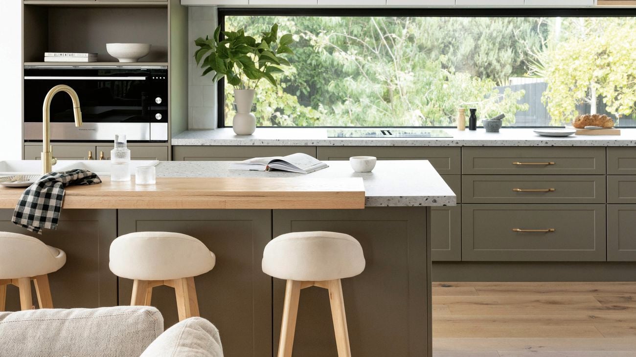 A kitchen with cabinets in dark beige and white, a long window above the bench