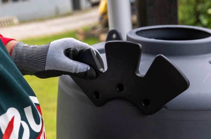 Hand wearing glove places hose hanger onto rainwater tank.