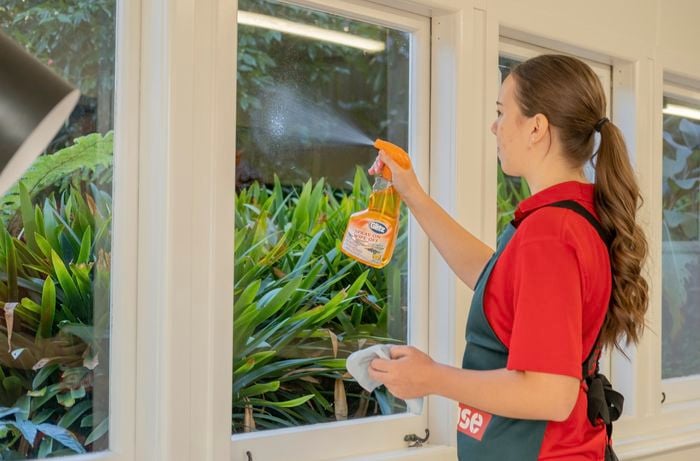 A Bunnings Team Member spraying a liquid onto a window and holding a cloth