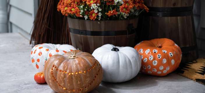 Close up of three decorated pumpkins in front of a potted plant in a barrel.