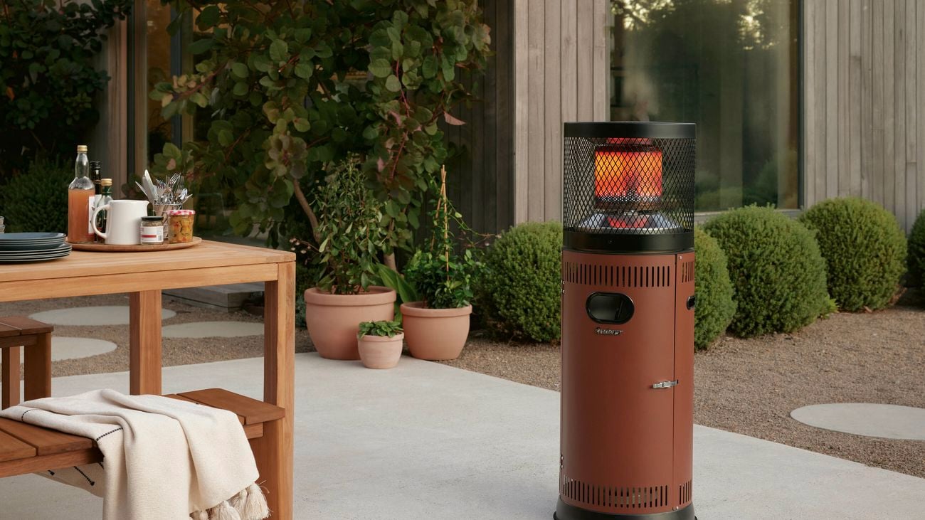 Rustic new outdoor patio heater sitting in a lovley patio area surrounded by green shrubs and outdoor setting