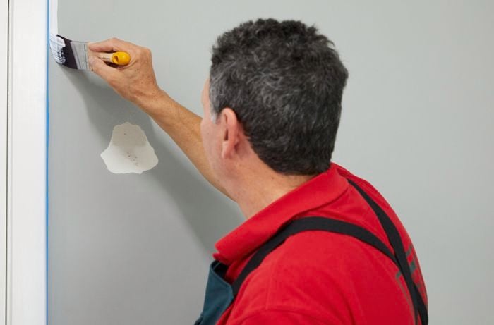 A man applies primer to an interior wall with an angled paintbrush.]