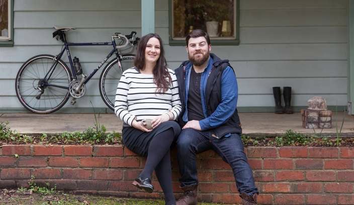 Woman and man sitting on brick fence out the front of a house.
