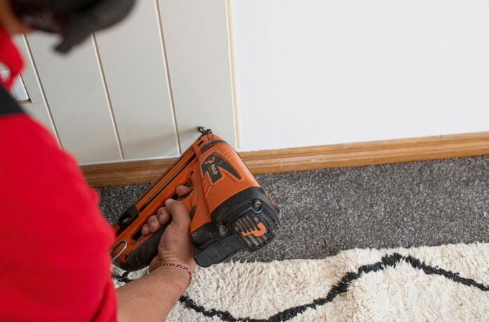 Person using a nail gun to fix the VJ feature wall panel securely in place against the wall.