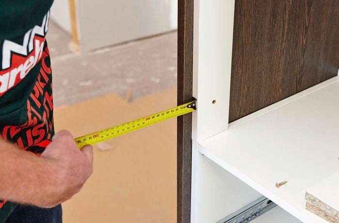 A person measuring the inset of a cabinet using a measuring tape