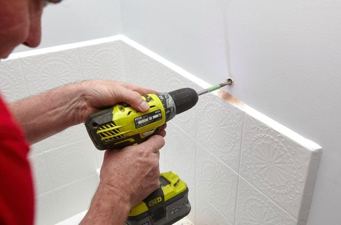 Person drilling a on screw into white bathroom wall.