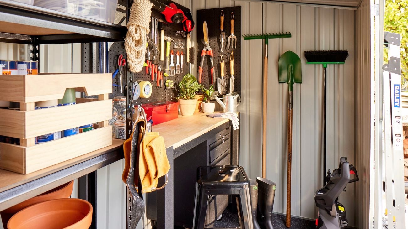 Interior of a garden shed facing hanging brooms and tools attached to a pegboard