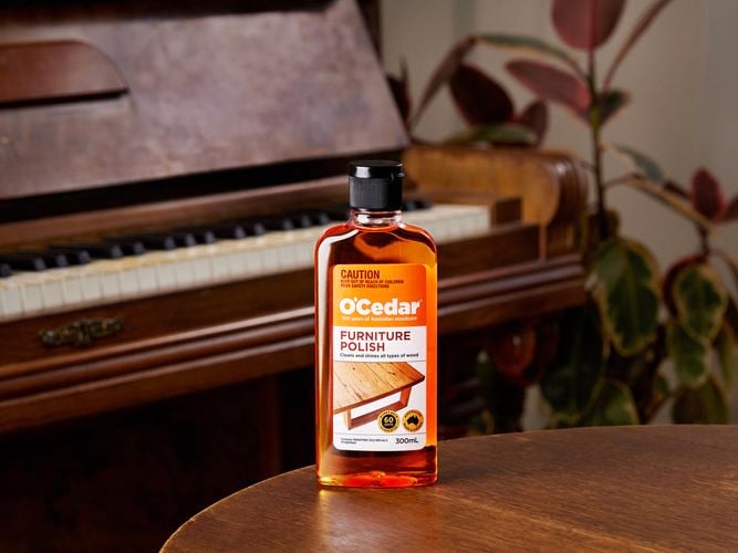 A bottle of O'Cedar Furniture Polish on a wooden table in front of a piano.