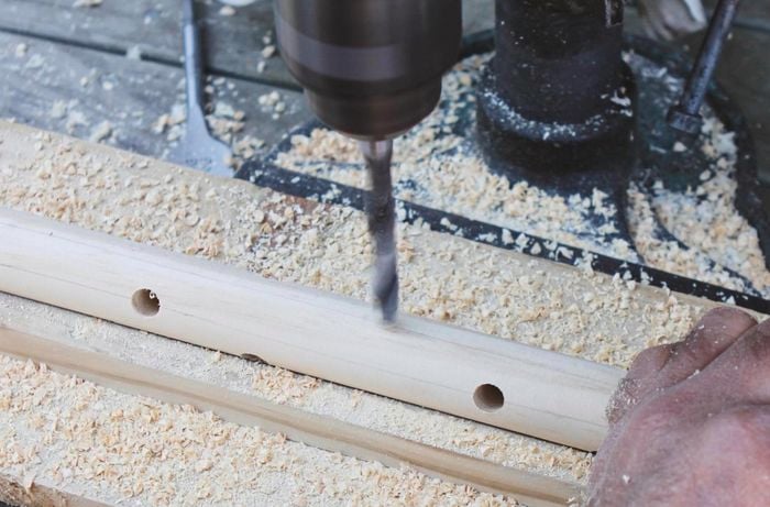 A length of dowel being drilled into to create branches of a dowel Christmas tree