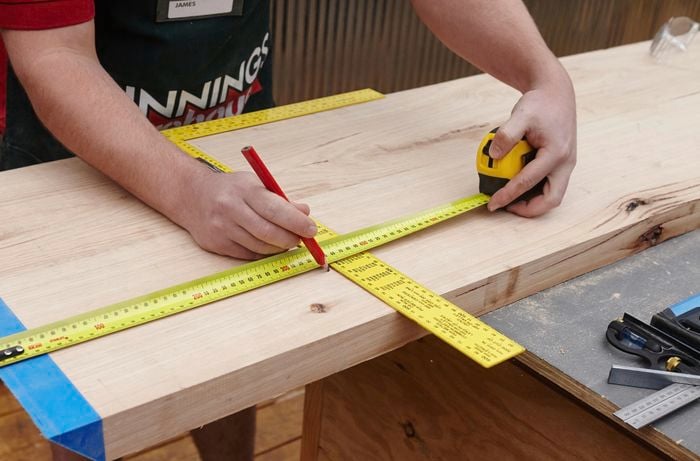 A person marking a piece of timber using a measuring tape and pencil