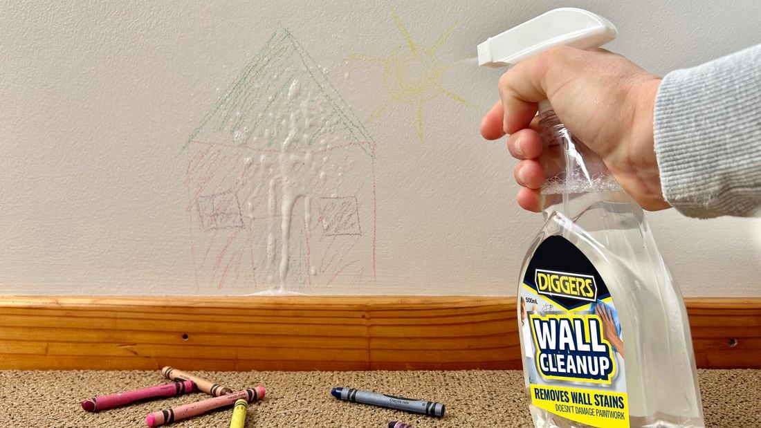 A person spraying wall cleanup to a wall with crayon drawings.