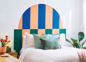 A D.I.Y. bed headboard in green, blue and apricot behind a double bed piled with pillows
