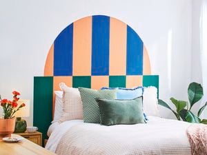 A D.I.Y. bed headboard in green, blue and apricot behind a double bed piled with pillows