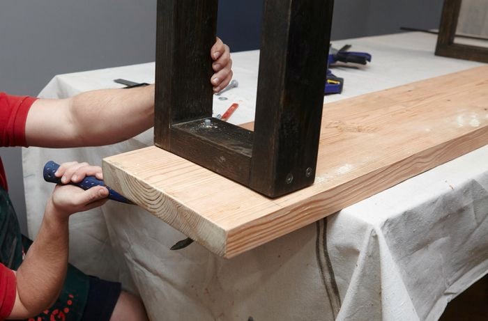 A person using a hammer to knock bolts through an upturned bench seat