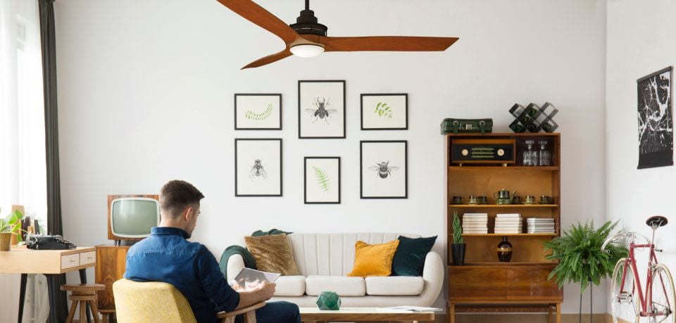 Person sitting in lounge room reading with timber desk, cabinet, white couch and wood veneer 3 blade ceiling fan