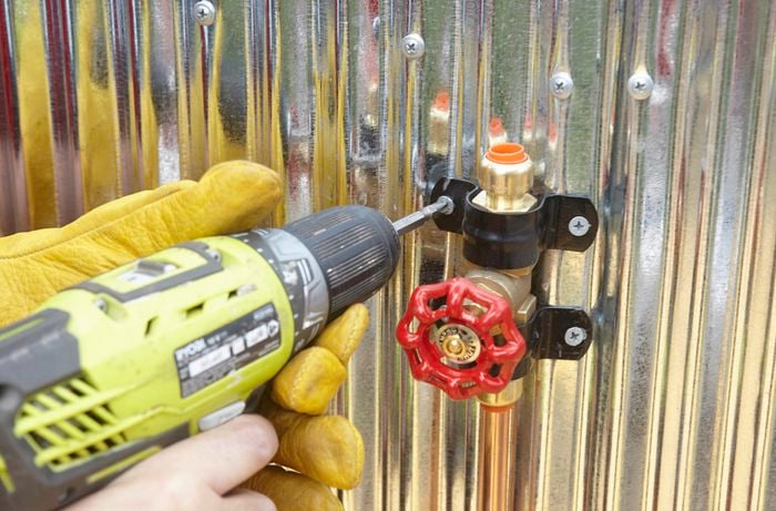 Person drilling brace into metal wall to hold tap in place.