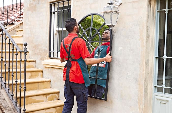 Two people holding either side of a large black-framed arch mirror to hang onto a wall