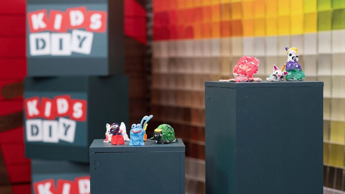 Cute clay creatures are displayed on pedestals with a colorful backdrop in Bunnings DIY workshop