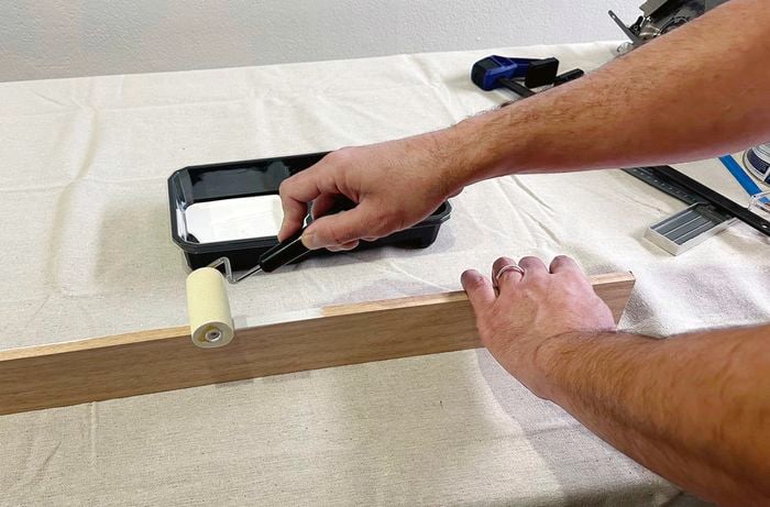 Left hand holds the timber rail in place while the other hand rolls white primer onto the top edge of the rail