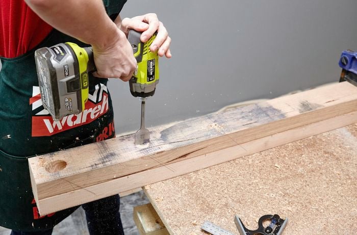 A power drill with a bore spade drill bit being used to drill a hole in two pieces of timber yb a Bunnings team member