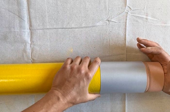 Hands joining a yellow cylinder, a silver paper ferrule, and a pink-painted foam plug.