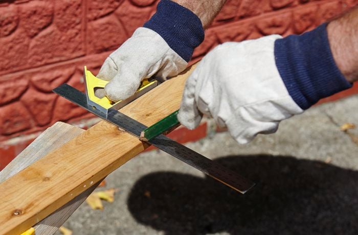 Person measuring bit of timber with steel ruler.