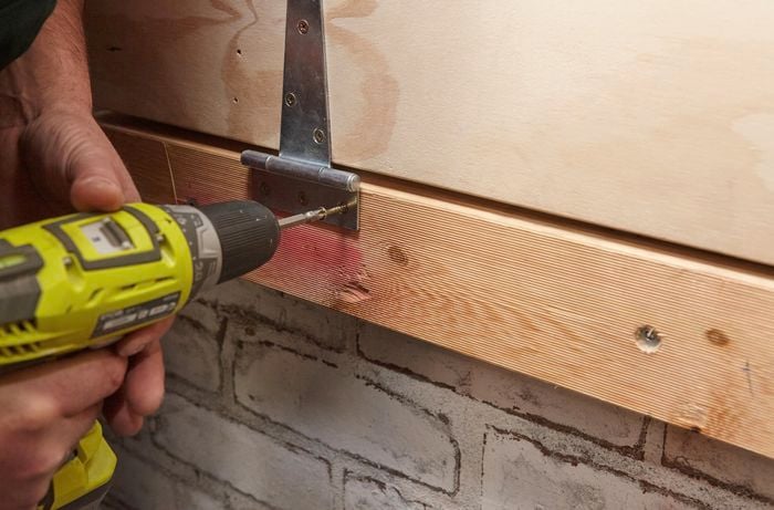 Person attaching hinge to wall using drill.
