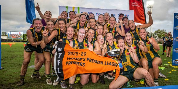 Women’s Premier League players celebrate a grand final victory on a football field, holding a premiership banner and trophy.