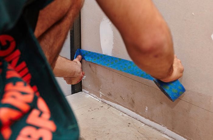 A person applying masking tape along a line drawn on a bathroom wall
