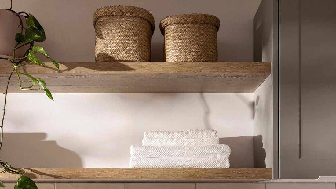 Open timber shelves with woven baskets, folded towels and trailing greenery.