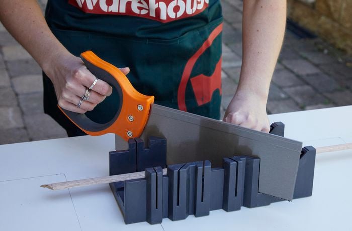 A person uses a mitre box and handsaw to cut a wood door trim