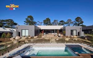 A backyard with a pool in it, lots of rocks, two water ranks and trees in it.
