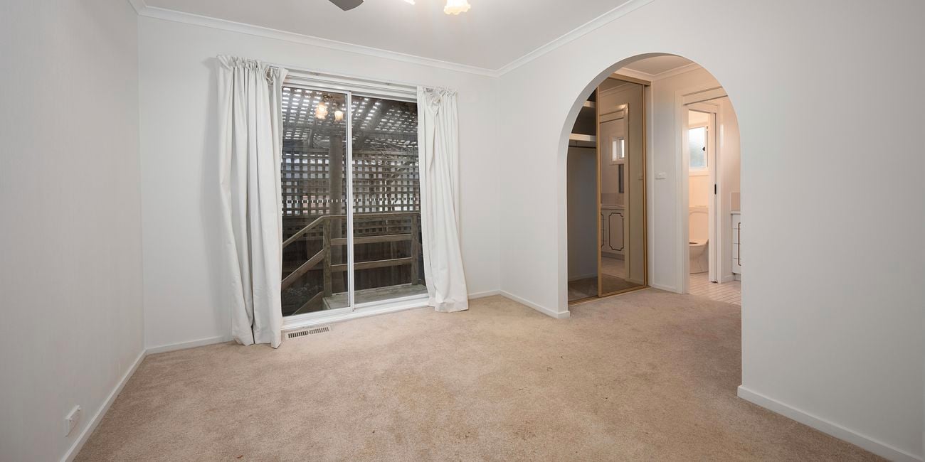 A room with carpet on the floor, ceiling fan, an archway and a glass sliding door to outside
