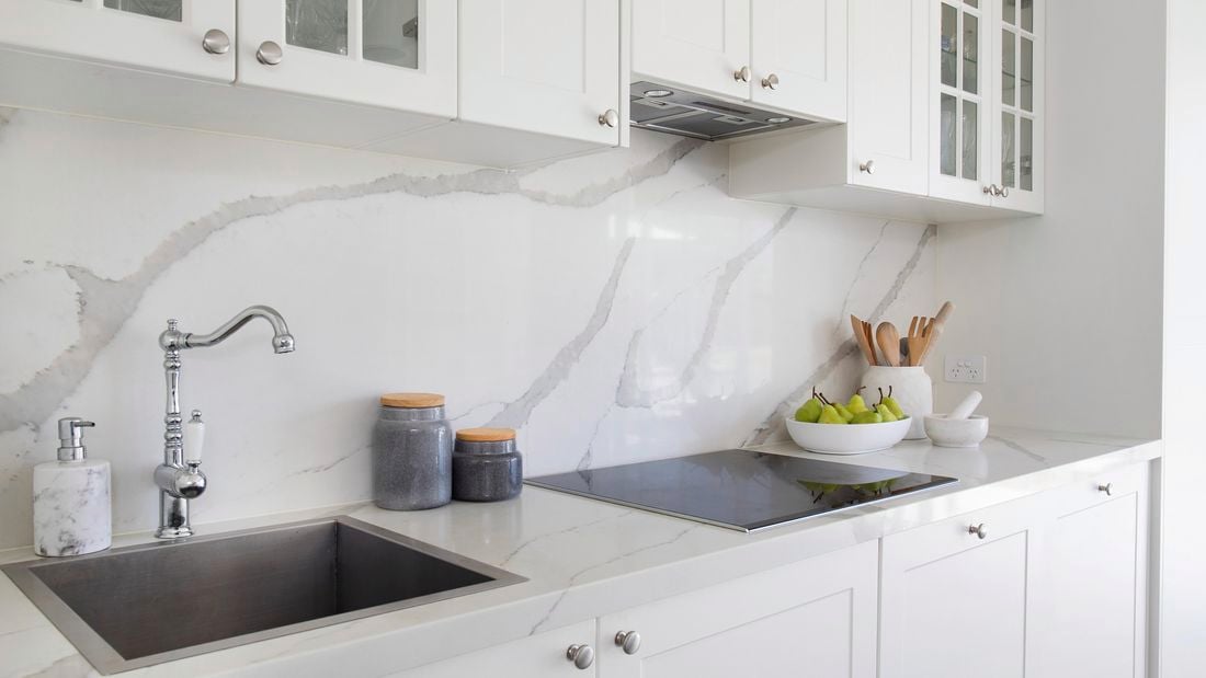 Modern white bathroom with white cabinetry, marble look splashback and benchtop, electric stovetop and stainless steel tapware.