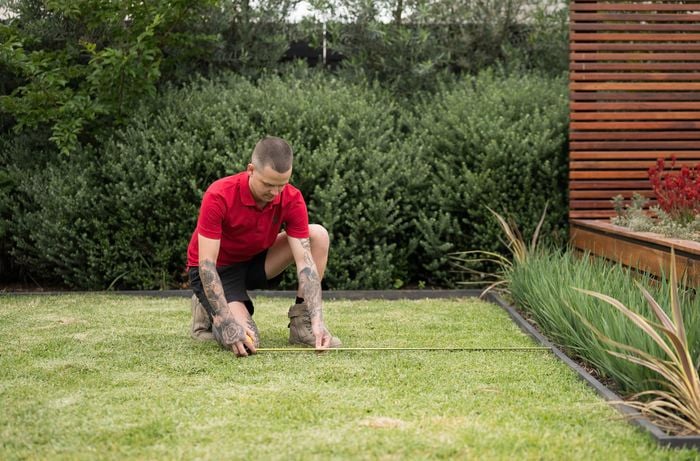 A Bunnings Team Member  is measuring the space using a tape measure to mark the dimensions for a raised garden bed.