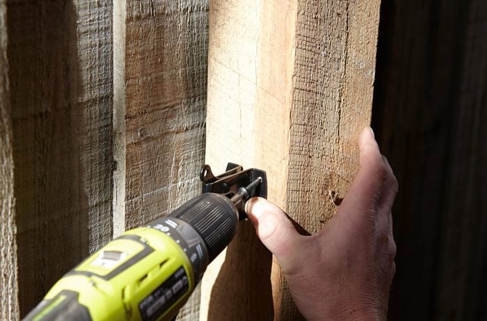 Person drilling gate latch into fence.