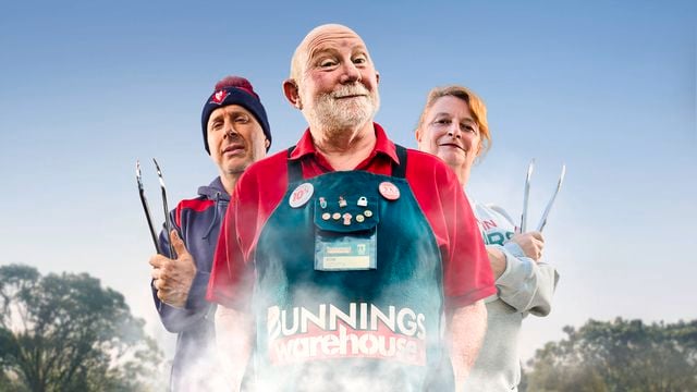 A Bunnings Team Member and 2 people in front of a BBQ with food on top of it.