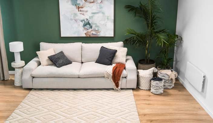 A painting on a wall in a lounge room, with a couch with cushions and a blanket on it, on a rug.