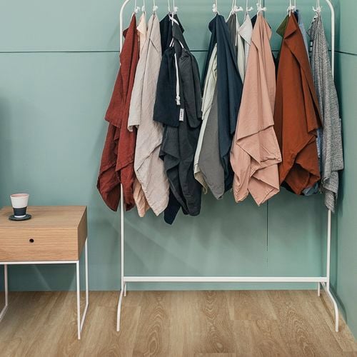 Clothes rack with small side table on floor boards with sage coloured walls.