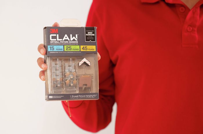 A person is holding a pack of claw picture hangers with different weight ratings to help choose the right hanger for framed artwork, mirrors and other wall décor. 